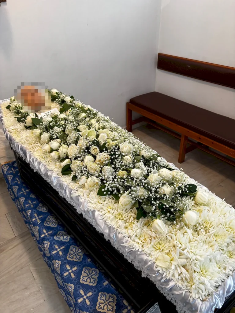 Απλός στολισμός φέρετρου με λευκά άνθη και λευκά τριαντάφυλλα.