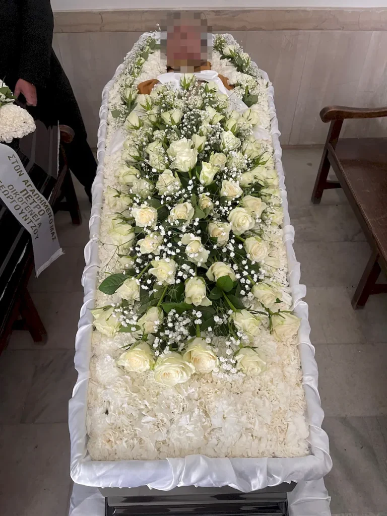 Απλός στολισμός φέρετρου με λευκά άνθη και λευκά τριαντάφυλλα.