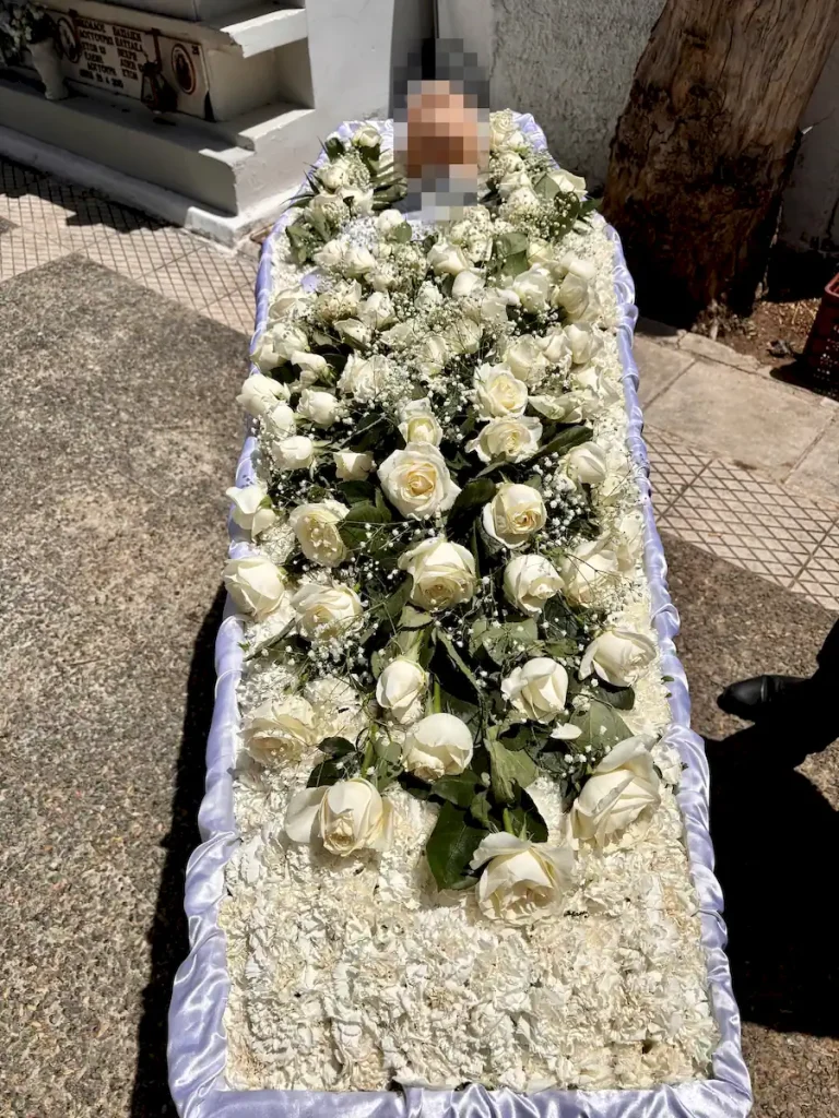 Απλός στολισμός φέρετρου με λευκά άνθη και λευκά τριαντάφυλλα.