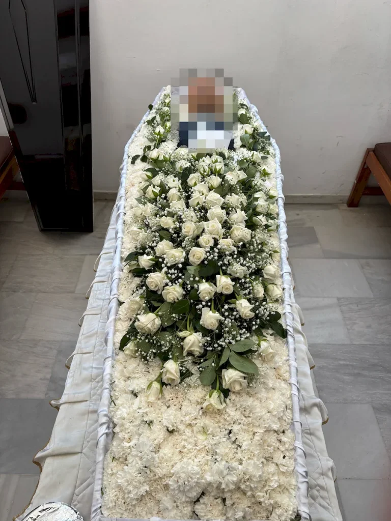 Απλός στολισμός φέρετρου με λευκά άνθη και λευκά τριαντάφυλλα.