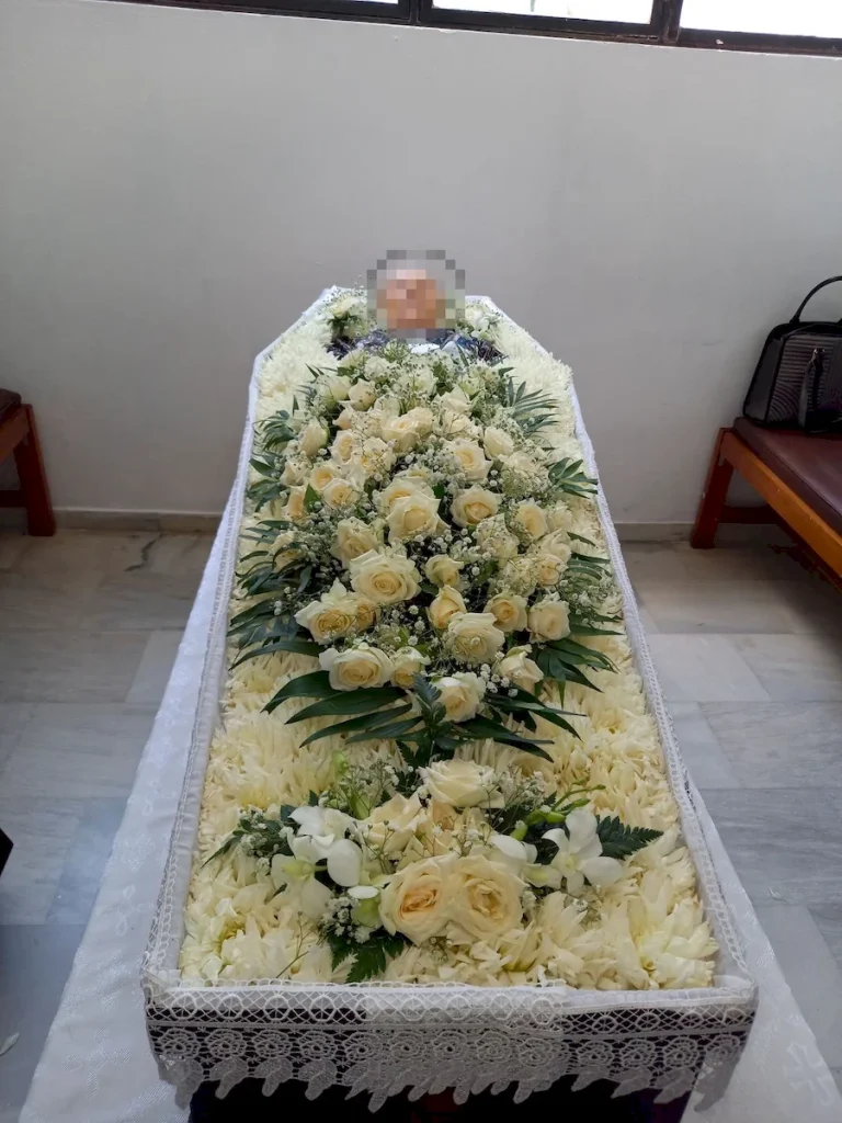 Απλός στολισμός φέρετρου με λευκά άνθη και λευκά τριαντάφυλλα.