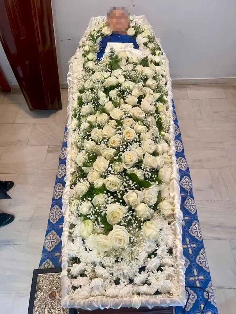 Απλός στολισμός φέρετρου με λευκά άνθη και λευκά τριαντάφυλλα.