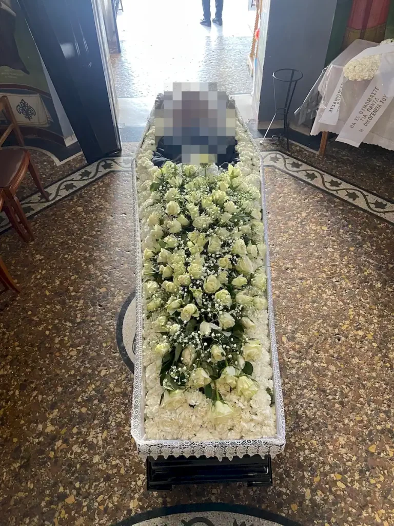 Απλός στολισμός φέρετρου με λευκά άνθη και λευκά τριαντάφυλλα.