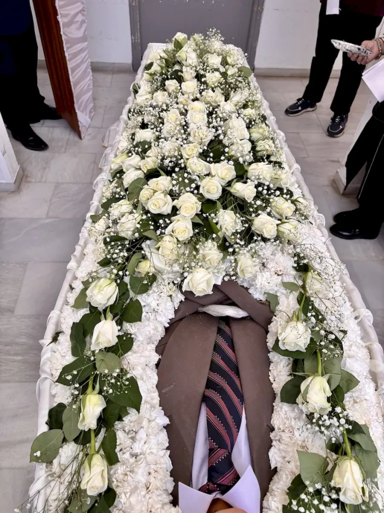 Απλός στολισμός φέρετρου με λευκά άνθη και λευκά τριαντάφυλλα.